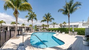 A swimming pool with a curved edge, surrounded by palm trees and lounge chairs. - "Tropical Oasis" by the beach & shops, with pool (Riviera Beach)