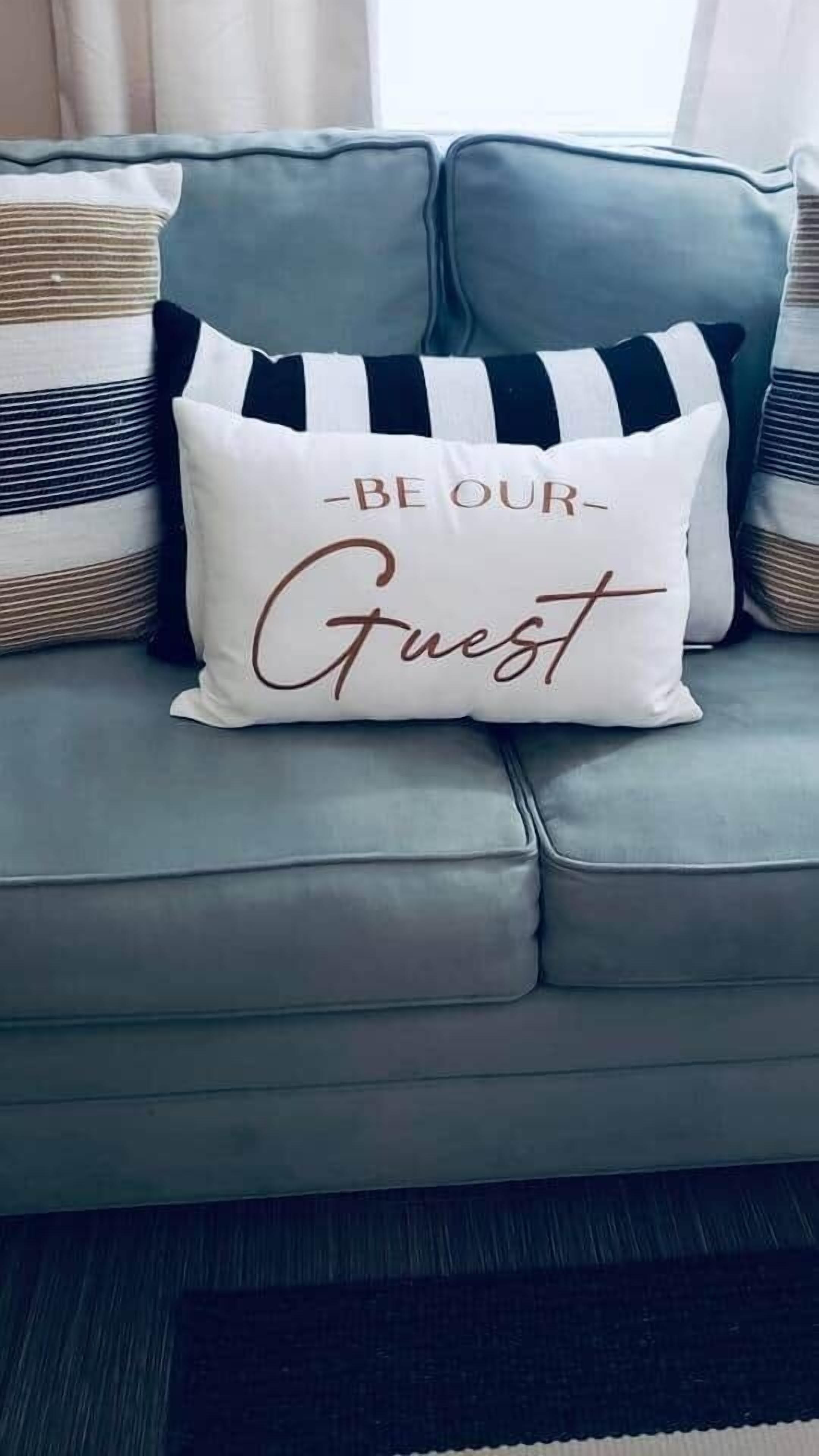 Un sofá gris con una almohada blanca que dice "BE OUR Guest".