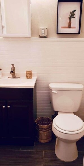 Une salle de bain avec des toilettes blanches, un meuble en bois foncé et un tableau encadré au mur.