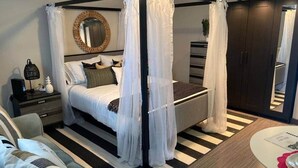 A bedroom with a four-poster bed, a round mirror, a dark wooden wardrobe, and a striped rug. - "Tropical Oasis" by the beach & shops, with pool (Riviera Beach)