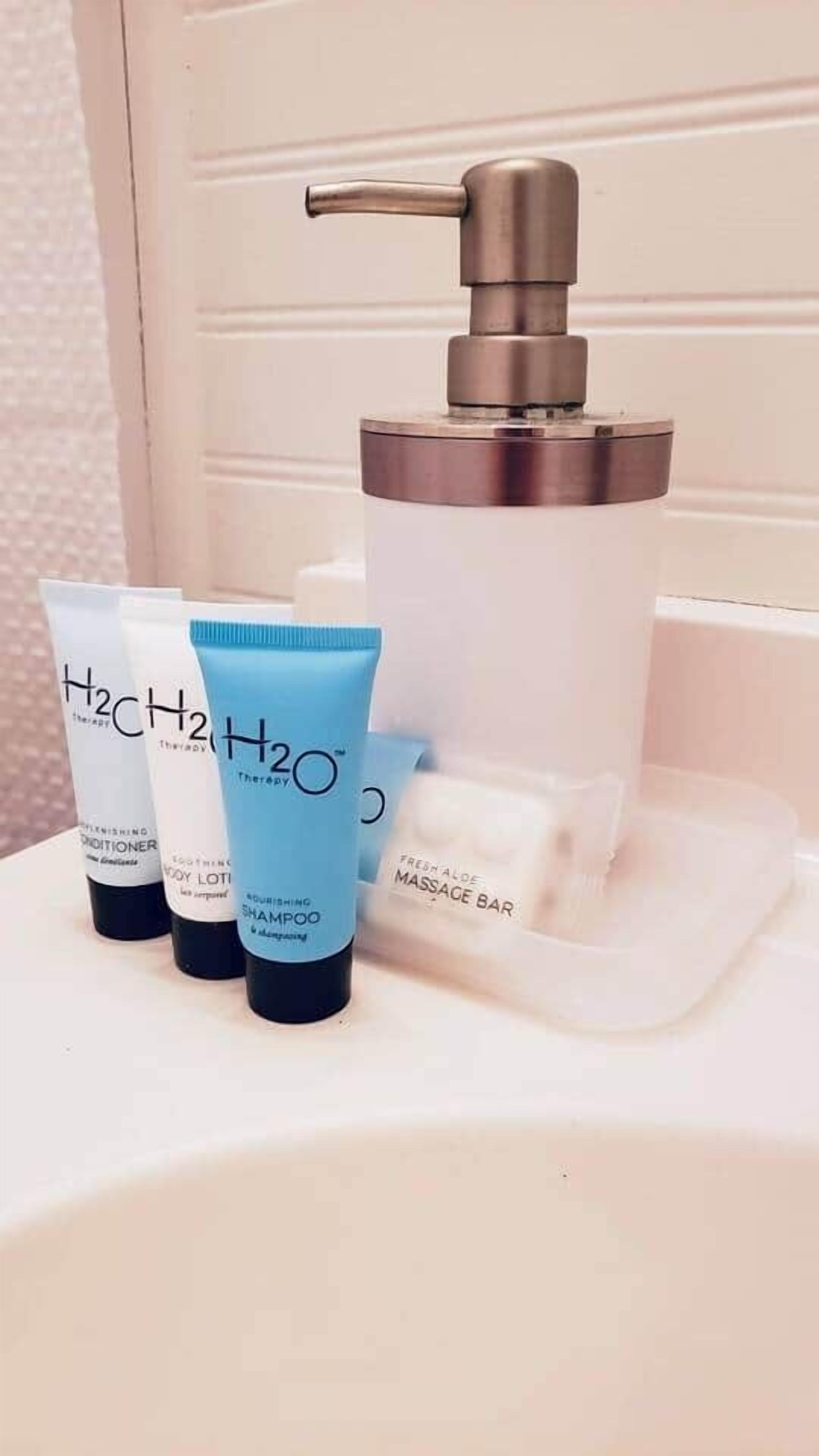 A bathroom sink with a hand soap dispenser, three tubes of H2O Therapy products, and a bar of soap.