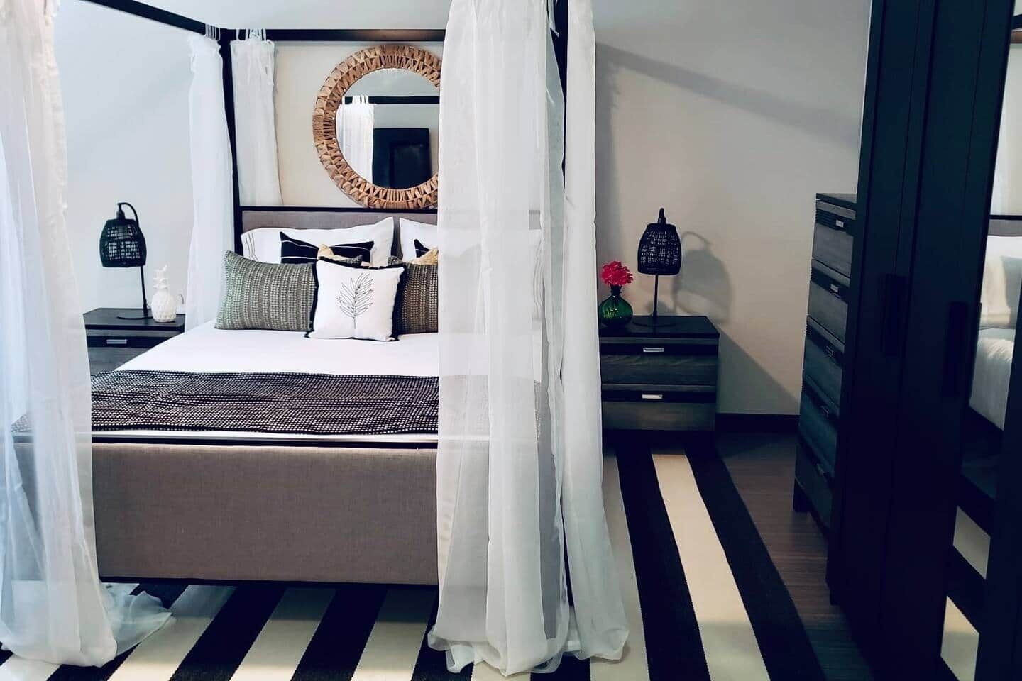 Une chambre à coucher avec un lit à baldaquin, une table de chevet avec une lampe, une commode et un miroir au mur.