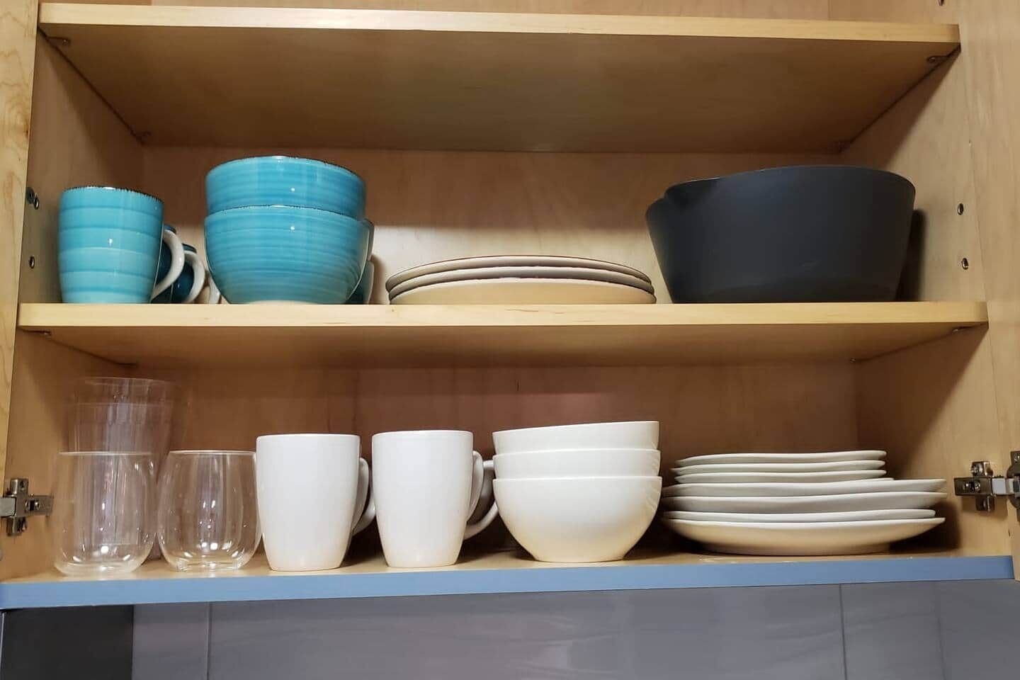 A kitchen cabinet with shelves holding various dishes and glassware.
