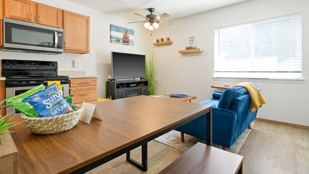 A modern kitchen with wooden cabinets, a microwave, and a dining area with a table and blue sofa. - Modern Downtown Kalispell Getaway — Walk to Coffee, Shops & Breweries (Kalispell)
