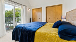 A bedroom with a bed, wooden wardrobes, a balcony with a railing, and a view of greenery outside. - Modern Downtown Kalispell Getaway — Walk to Coffee, Shops & Breweries (Kalispell)