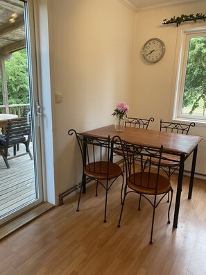 A dining area with a wooden table and metal chairs, a vase with flowers, a clock on the wall, and a window with a view of greenery. - Traditional Swedish wooden house by Lake Torsjön  (Ingelstad, Växjö)