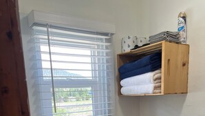 Een badkamer met een raam, een wastafel, een toilet en een plank met handdoeken.