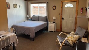 Een slaapkamer met een bed, nachtkastjes, een stoel, een tafel, een deur en een raam.