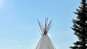Una tienda tipi blanca con una entrada central, ubicada sobre una superficie de grava y un banco cerca.
