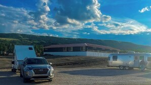 Una casa moderna con un amplio camino de entrada, un coche aparcado y una caravana en un entorno rural.