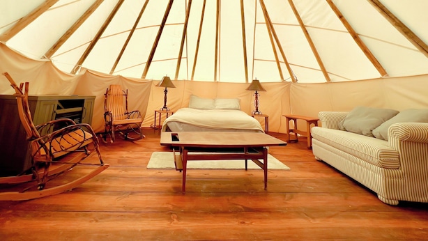 Un interior espacioso con una cama, una mesa de madera, un sillón mecedora y un sofá a rayas.