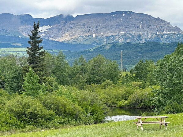 A picnic table in a grassy area with a river and mountains in the background.