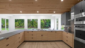 Eine moderne Küche mit Holdekor, Edelstahlgeräten und großen Fenstern mit Blick auf Grünflächen.