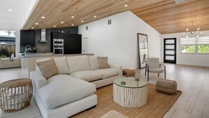 Ein geräumiger Wohnbereich mit moderner Küche, einem großen Sofa, einem runden Couchtisch und Blick ins Freie.