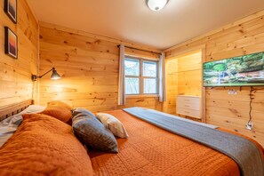 A cozy wooden cabin room with a bed, a TV, and a window with curtains.
