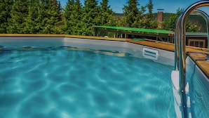 En swimmingpool med krystalklart, blåt vand, omgivet af en træterrasse og en bygning med grønt tag.