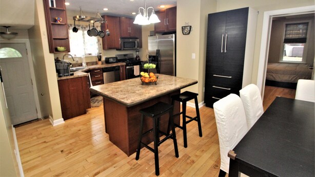 Una cocina moderna con armarios de madera, una isla central y un comedor con una mesa negra y sillas blancas.