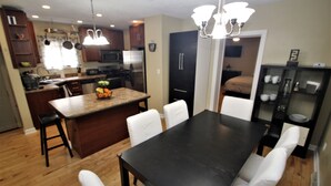 Una cocina moderna con armarios de madera, una isla central y un comedor con mesa oscura y sillas blancas.