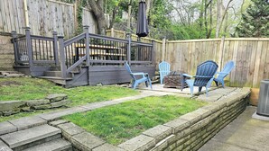 Un patio trasero con una terraza de madera, un muro de contención de piedra y sillas Adirondack azules.