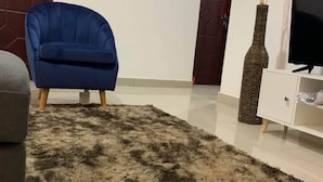 Una sala de estar con un sillón azul, un sofá gris, una alfombra mullida, un mueble blanco y un televisor.