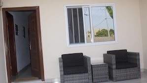 Una habitación con una puerta de madera, una ventana que da a zonas verdes y dos sillas de mimbre.