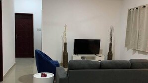 Una sala de estar moderna con un sofá gris, un sillón azul, una mesita auxiliar blanca y un televisor de pantalla plana sobre un soporte blanco.