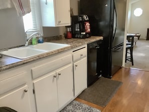 A kitchen with white cabinets, a black refrigerator, a coffee maker, and a sink.