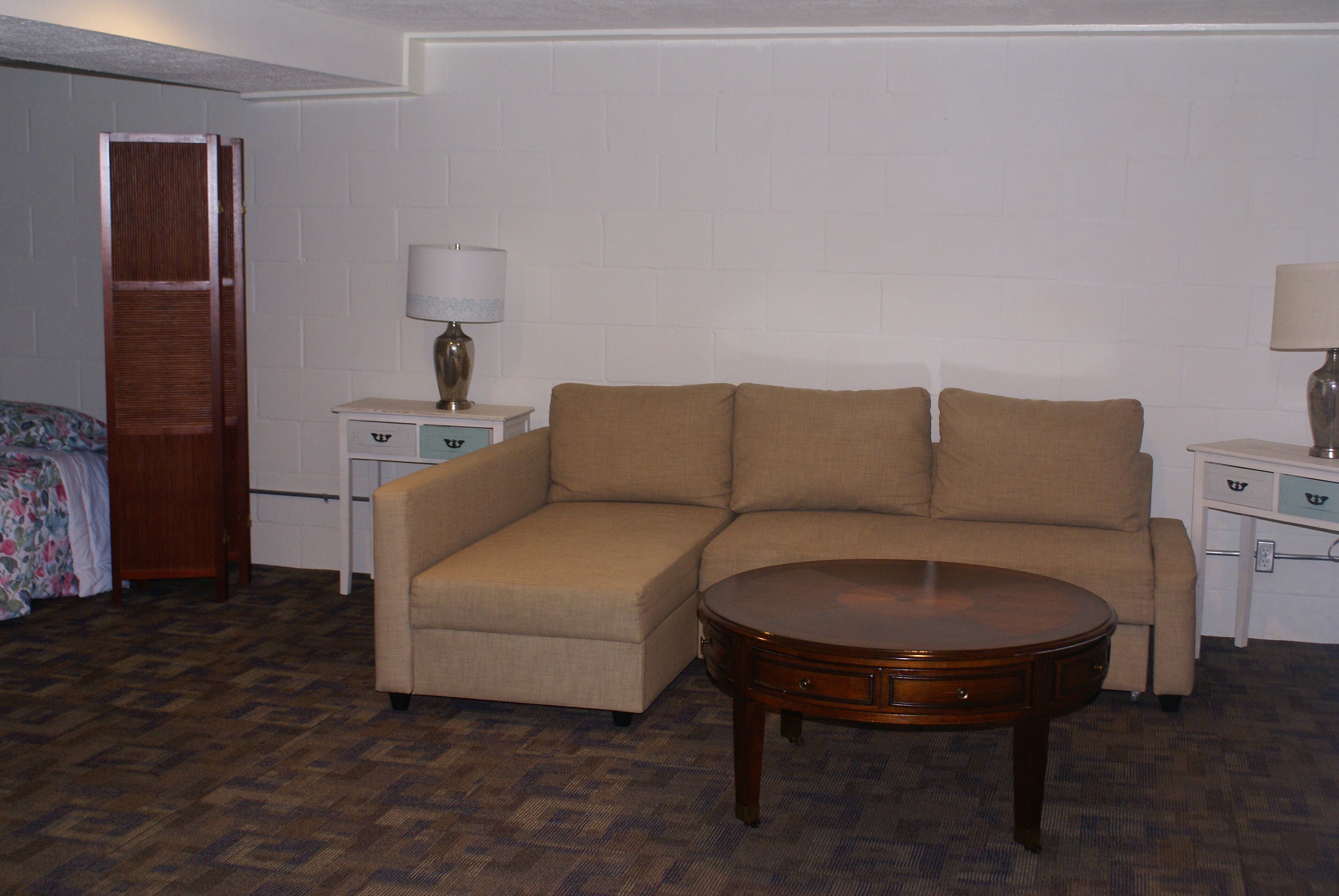 Una habitación con un sofá seccional color beige, una mesa de centro de madera y dos mesitas de noche con lámparas.