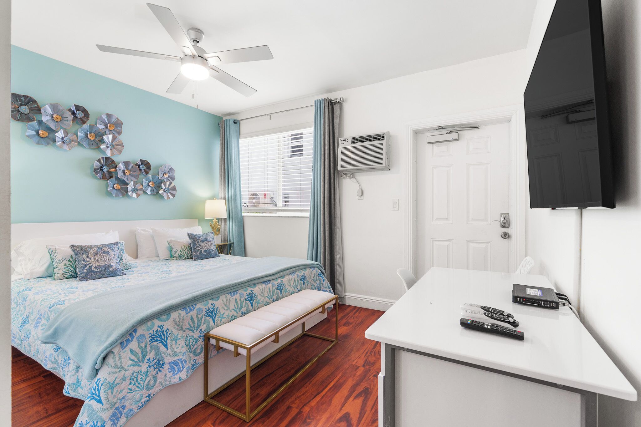 Une chambre à coucher comprenant un lit, une table de chevet, un ventilateur de plafond, un appareil de climatisation et un téléviseur fixé au mur.