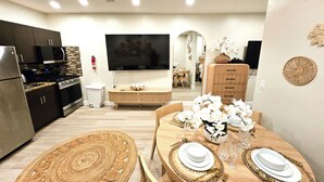A modern kitchen with dark cabinetry, a built-in microwave, and a stove. There is a dining area with a wooden table set for two, white plates, and a vase of white flowers.