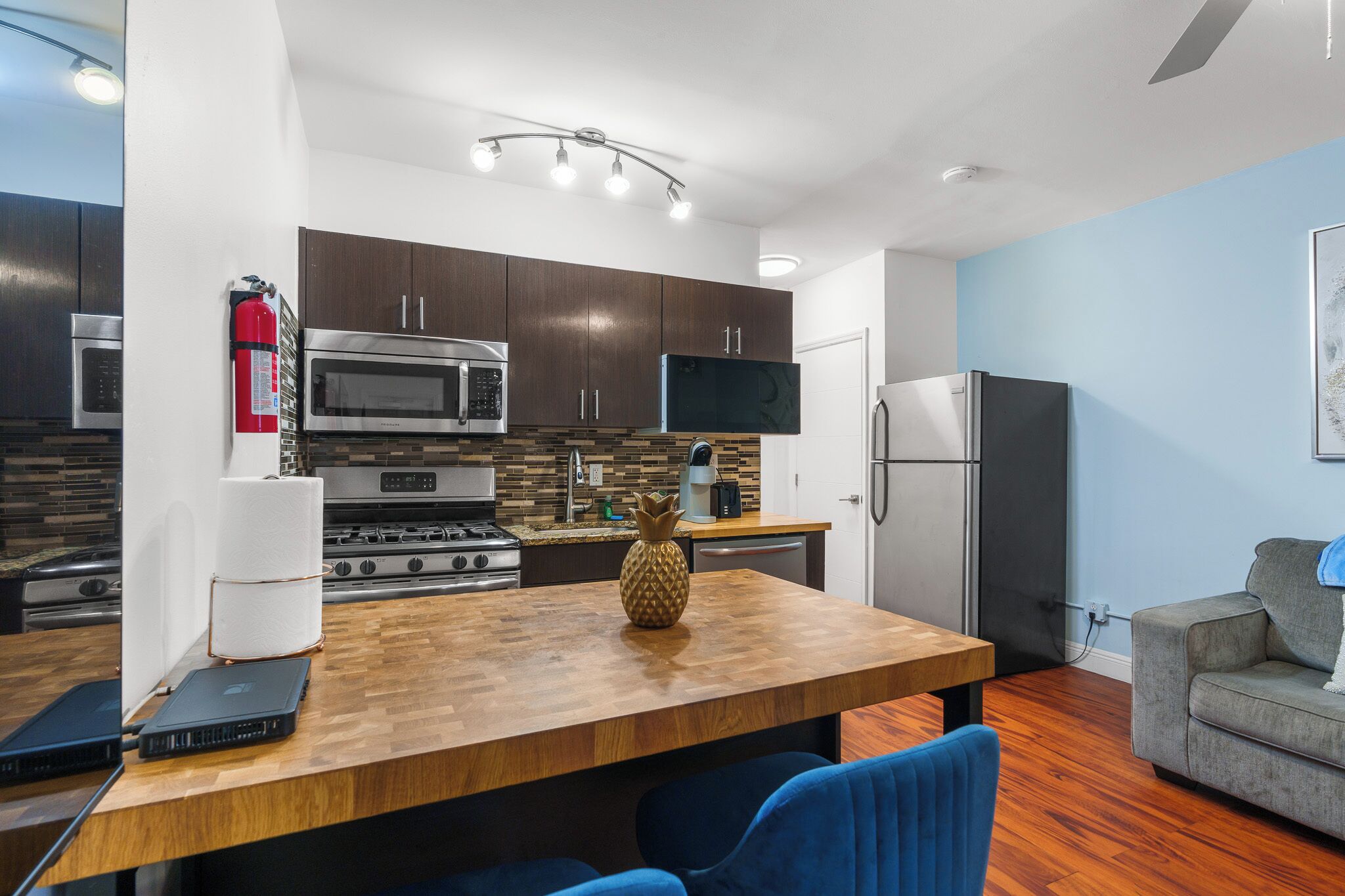 A modern kitchen with dark wooden cabinets, stainless steel appliances, and a wooden island with a pineapple centerpiece.