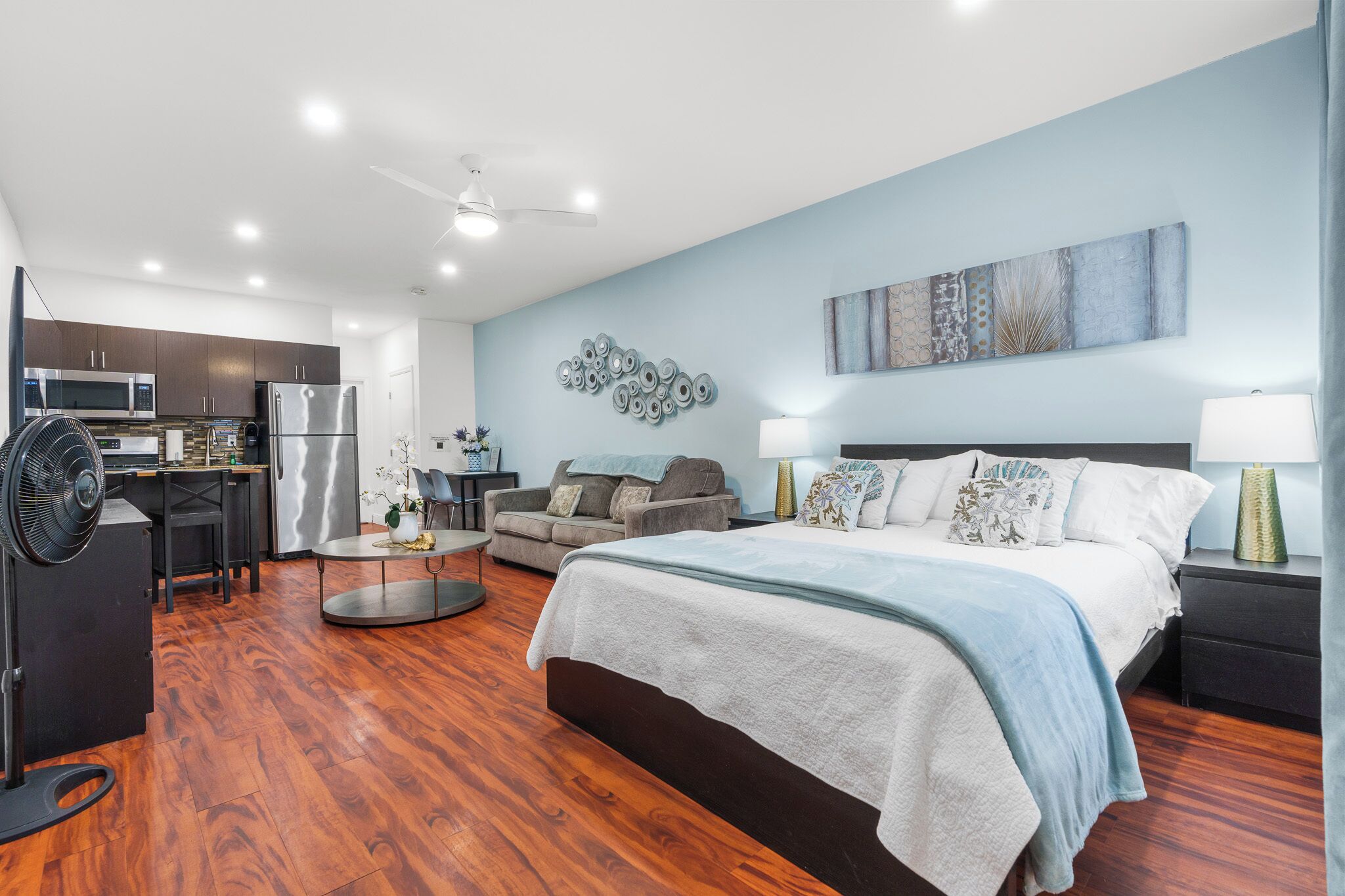 A modern hotel room with a bed, a sofa, a dining area, and a kitchen.
