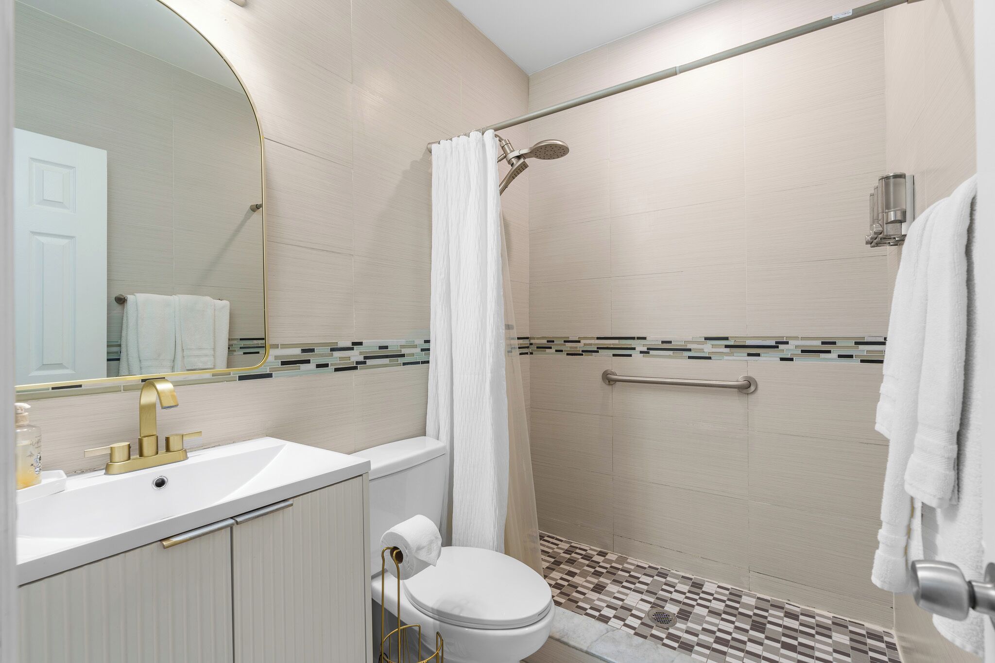 A modern bathroom with a white sink, gold faucet, and a shower with a glass door.