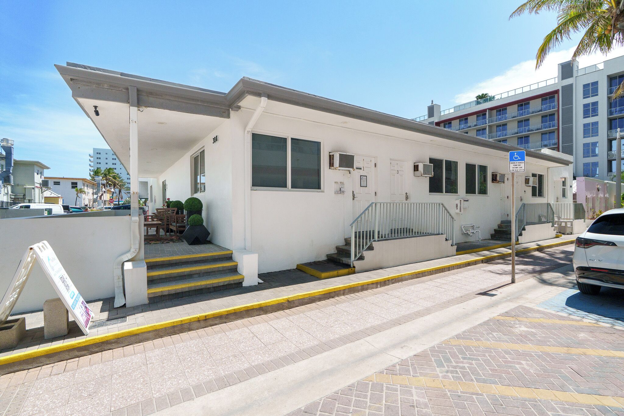 Un edificio blanco con un acceso cubierto, una rampa accesible para sillas de ruedas y una zona de estacionamiento.