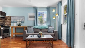A modern living room with a grey sofa, wooden coffee table, and a view of the outside through a window with blue curtains.