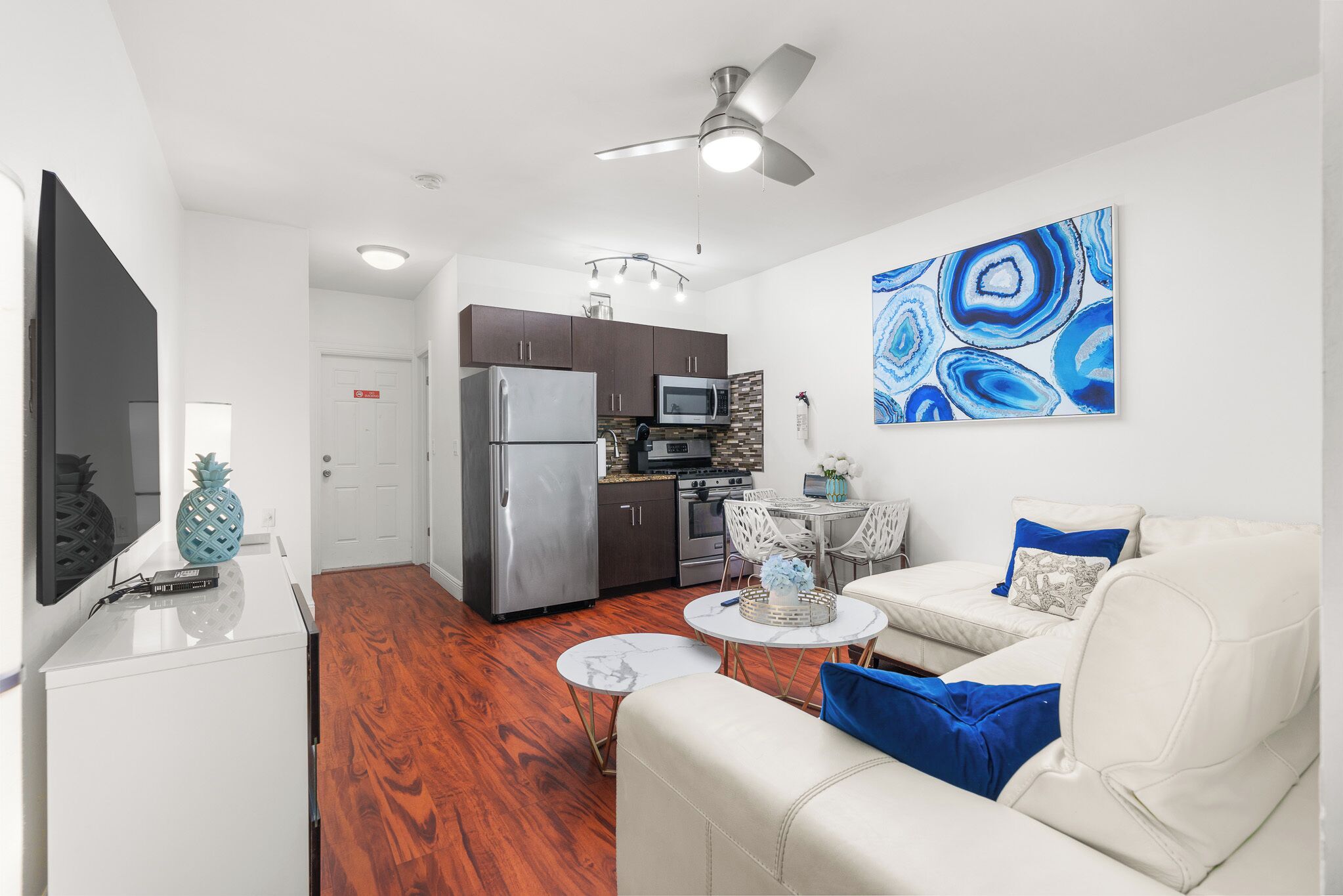 A modern living room with a white sofa, a coffee table, and a kitchen area with dark cabinets and stainless steel appliances.