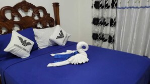 Ein ordentlich bezogenes Bett mit blauen Laken, weißen Kissen mit Logos und einem Zierhandtuch.