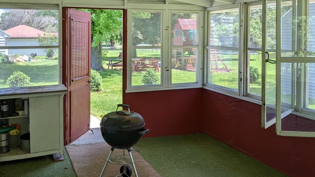 Una habitación con ventilador de techo, ventanas amplias y una parrilla.