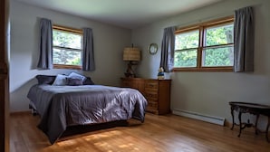 Un dormitorio con cama, cómoda y dos ventanas.