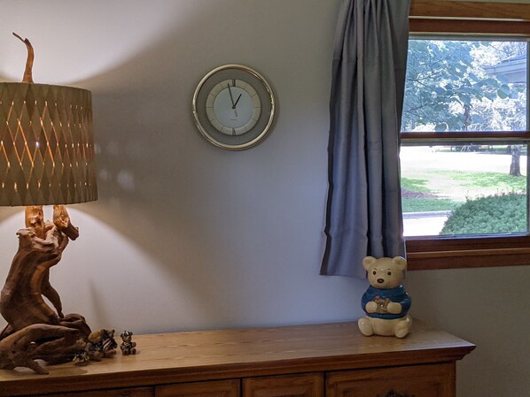 Un aparador de madera con un reloj, una lámpara y un osito de peluche.