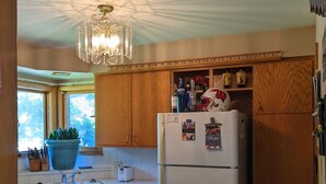 Una cocina con armarios de madera, un refrigerador blanco, una araña y una ventana con una planta en maceta.