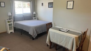 Ein Schlafzimmer mit einem Bett, Nachttischen, einem Tisch mit Stühlen und einem fenster mit Vorhängen.