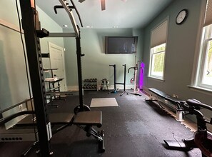 Work out in comfort with a home gym featuring a squat rack, bench press, stationary bike, dumbbells, and resistance bands.