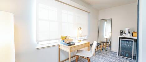 A room with a desk, chair, window, and a refrigerator.