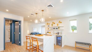 A modern kitchen with a marble island, wooden chairs, pendant lighting, and a built-in dishwasher.