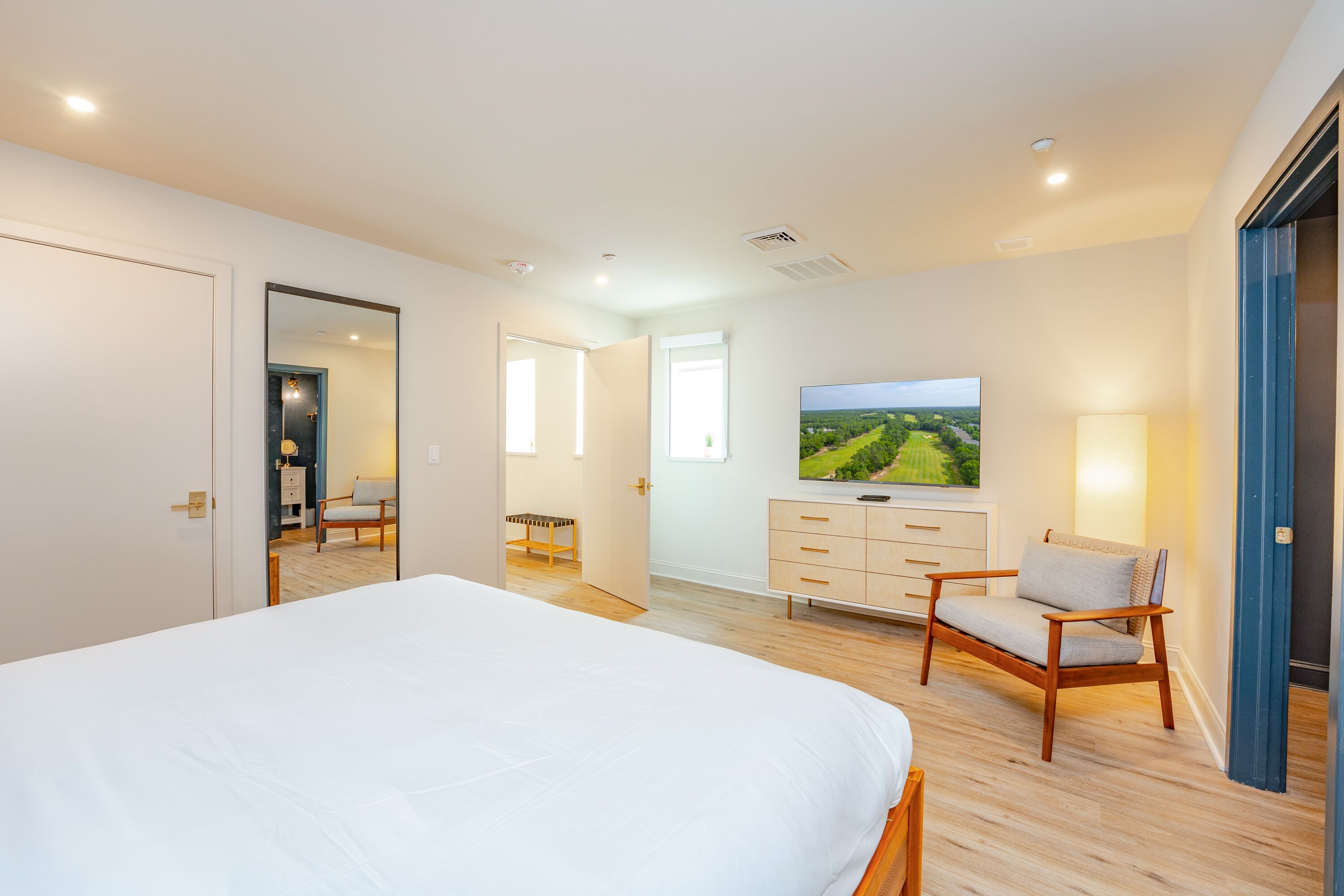 A modern bedroom with a large bed, a television, a dresser, and a chair.
