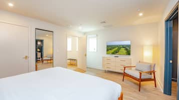 A modern bedroom with a large bed, a television, a dresser, and a chair.