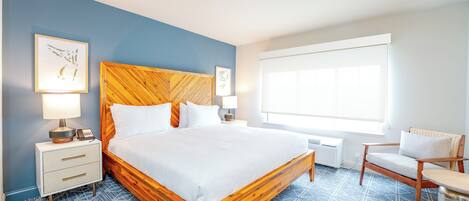 A hotel room with a wooden bed, a nightstand with a lamp, a chair, and a large window.