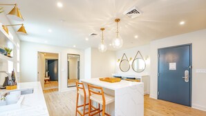 A modern kitchen with a marble island, wooden bar stools, pendant lighting, and a blue door.
