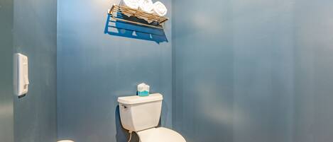 Un baño con inodoro, toallero con toallas y dispensador de papel higiénico.